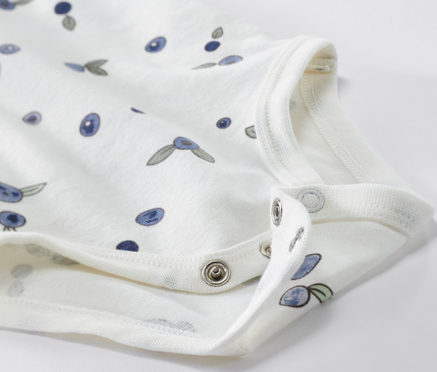 Egy fehér, áfonyás mintájú, hosszú ujjú baba body közelképe.