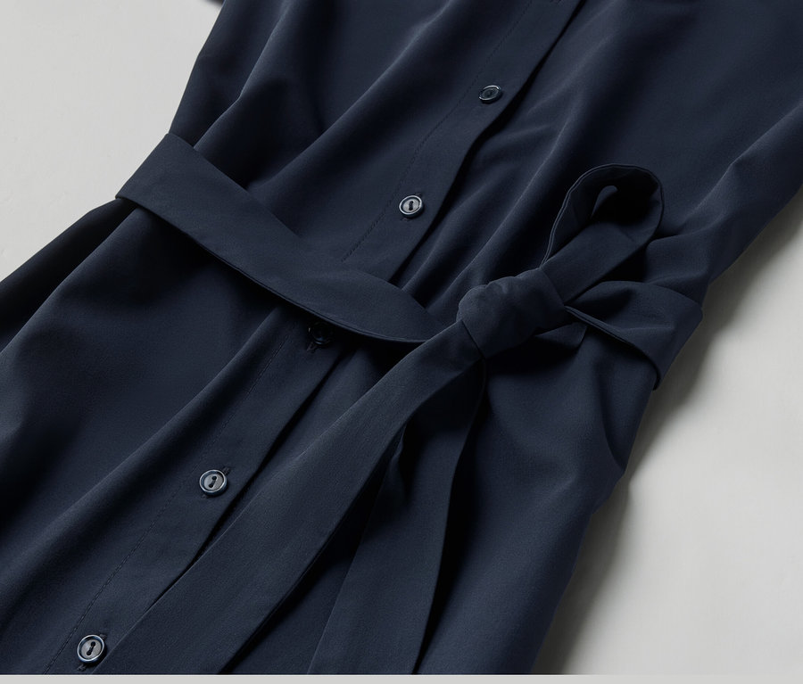 Egy sötétkék, gombos, öves női funkcionális ruha közeli képe.