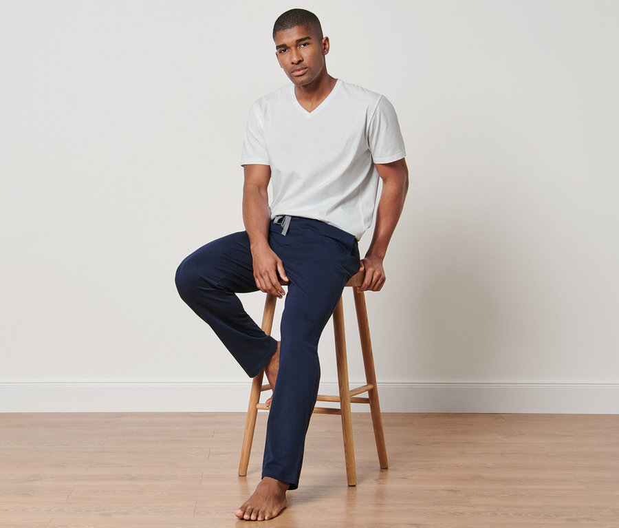 Férfi ül egy széken, fehér pólót és sötétkék nadrágot visel egy 4 részes pizsama szettből.