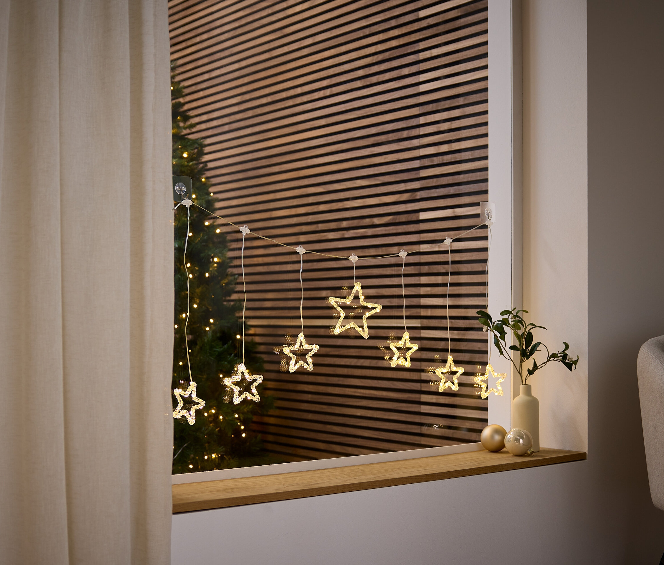 Csillag alakú fényfüzér lóg az ablakban, mögötte karácsonyfa látható.