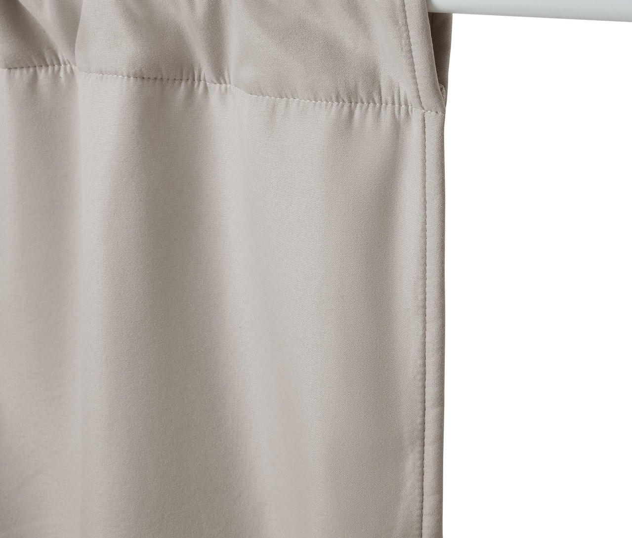 Bézs függöny lóg egy fehér rúdon.
