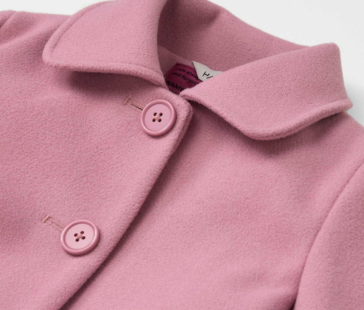 Egy rózsaszín kabát részlete gallérral és gombokkal.