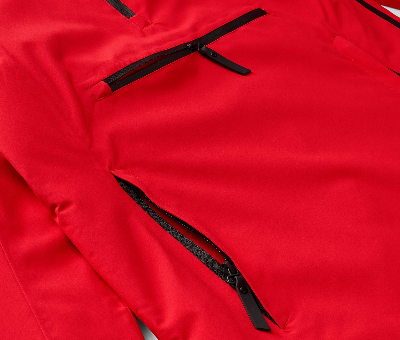 Egy piros kabát részlete fekete cipzárakkal a zsebeken.