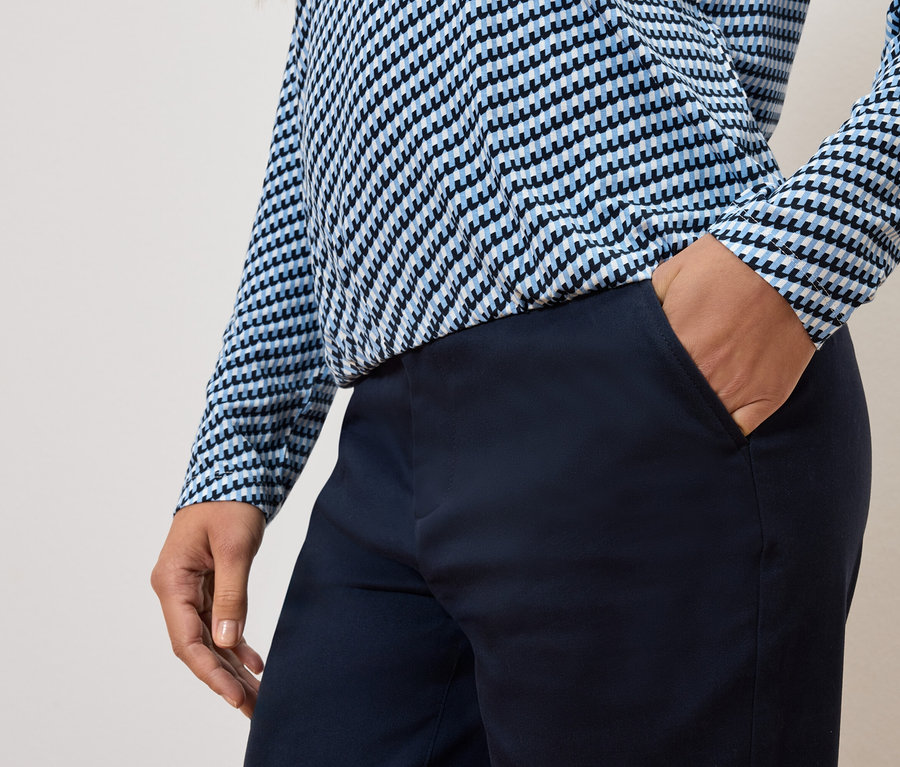 Részleges nézet egy személyről, aki kezét a nadrágzsebébe tette és kék-fehér felsőt visel.