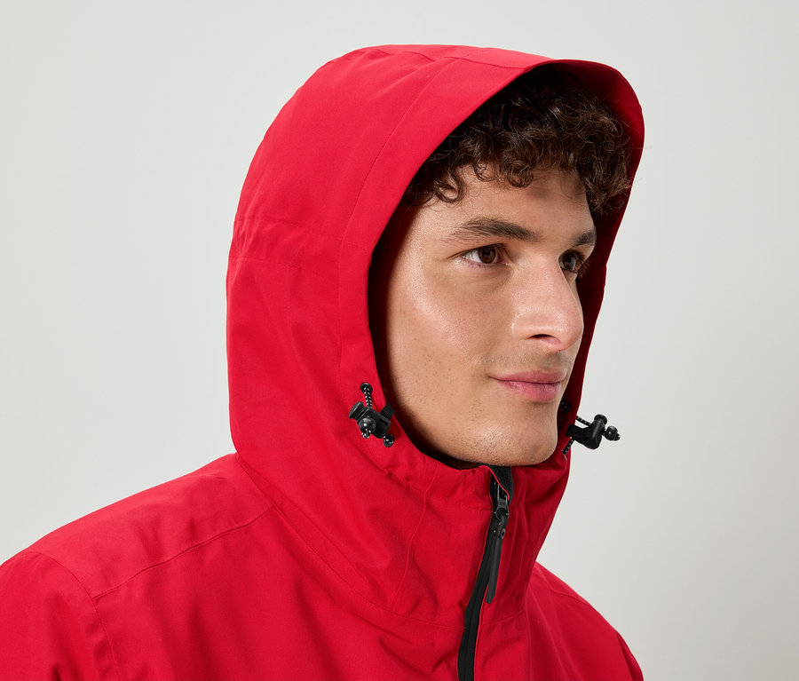 Egy göndör hajú férfi piros kapucnis kabátot visel.