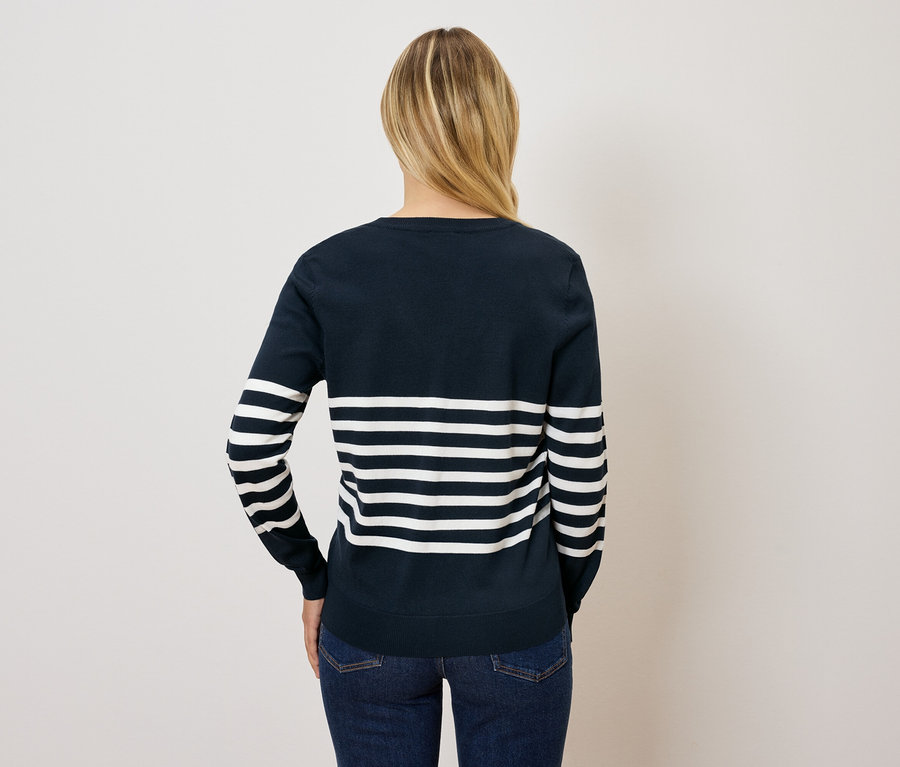 Hátulról látható egy szőke hajú nő kék-fehér csíkos pulóverben és farmerban.