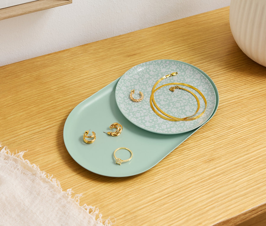 Arany ékszerek fekszenek dekoratív tányérokon egy fa asztalon.