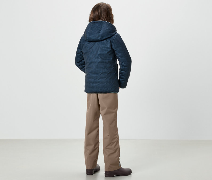 Egy fiú háttal áll a kamerának, kék kabátot és Kinder-Regenhose esőnadrágot visel.