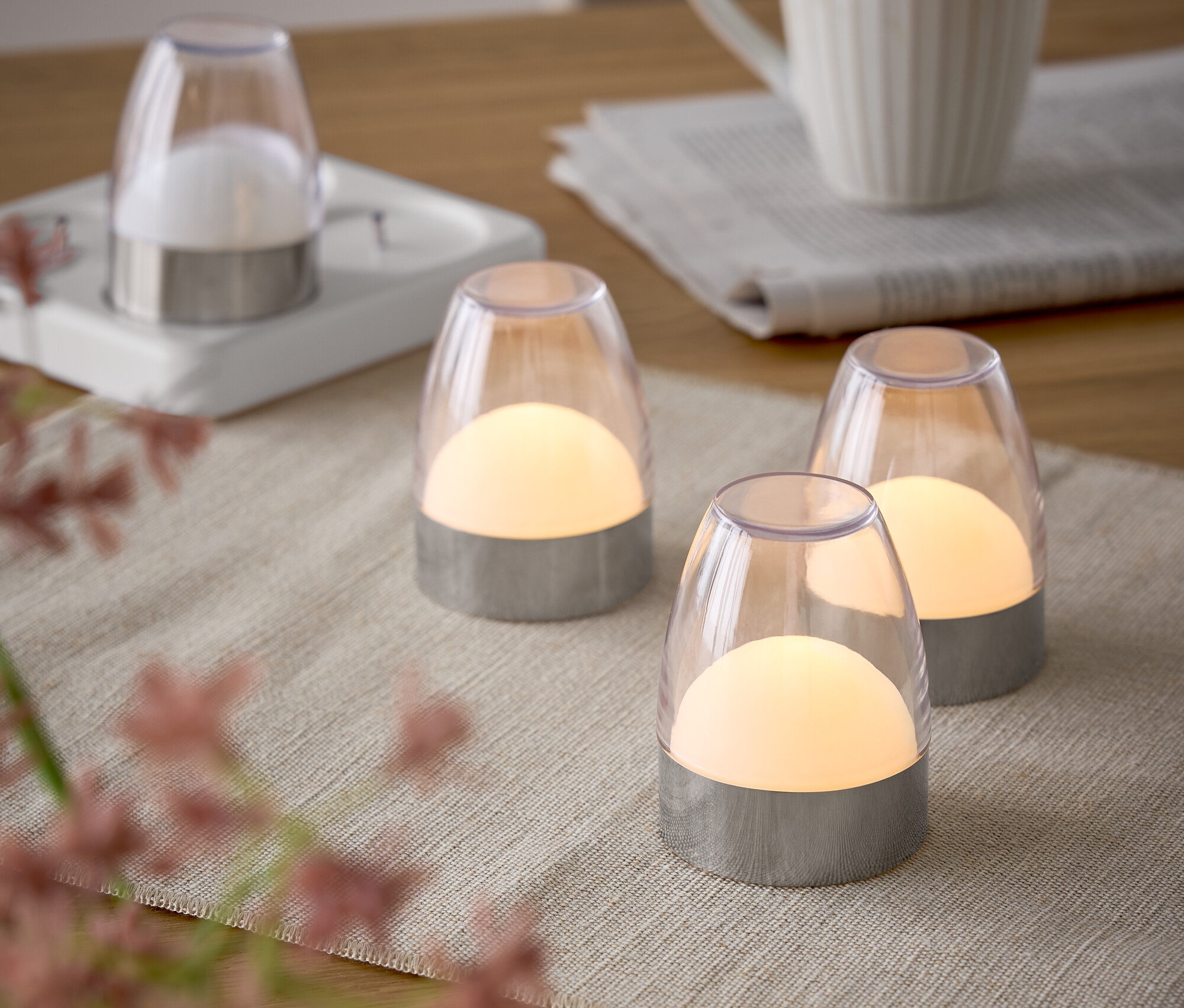 Négy lámpa egy asztalon asztalterítővel, egy csésze és egy újság mellett.