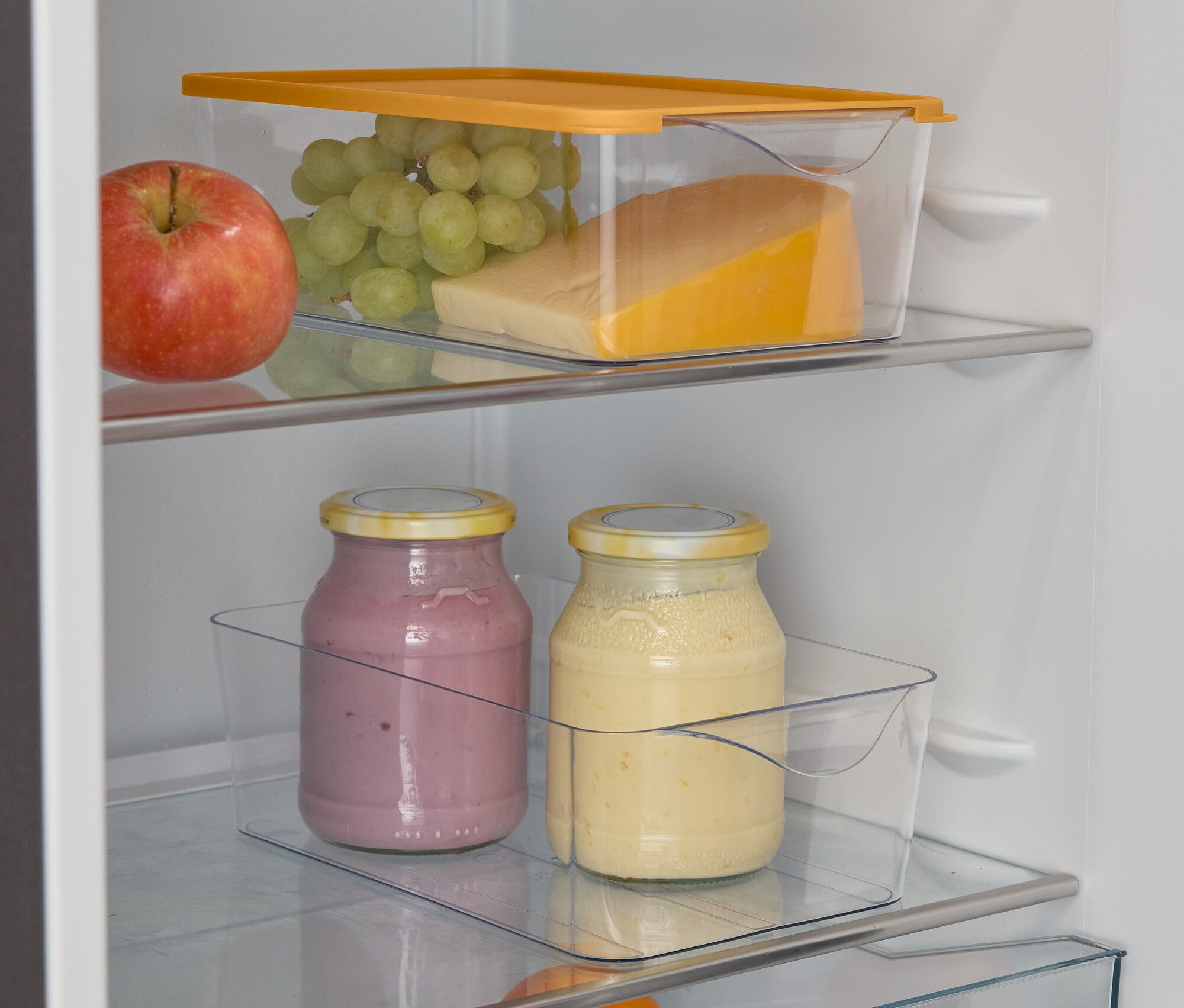 Egy nyitott hűtőszekrény alma, szőlő, sajt, két smoothie-s pohár, egy narancs és lime-ok társaságában.