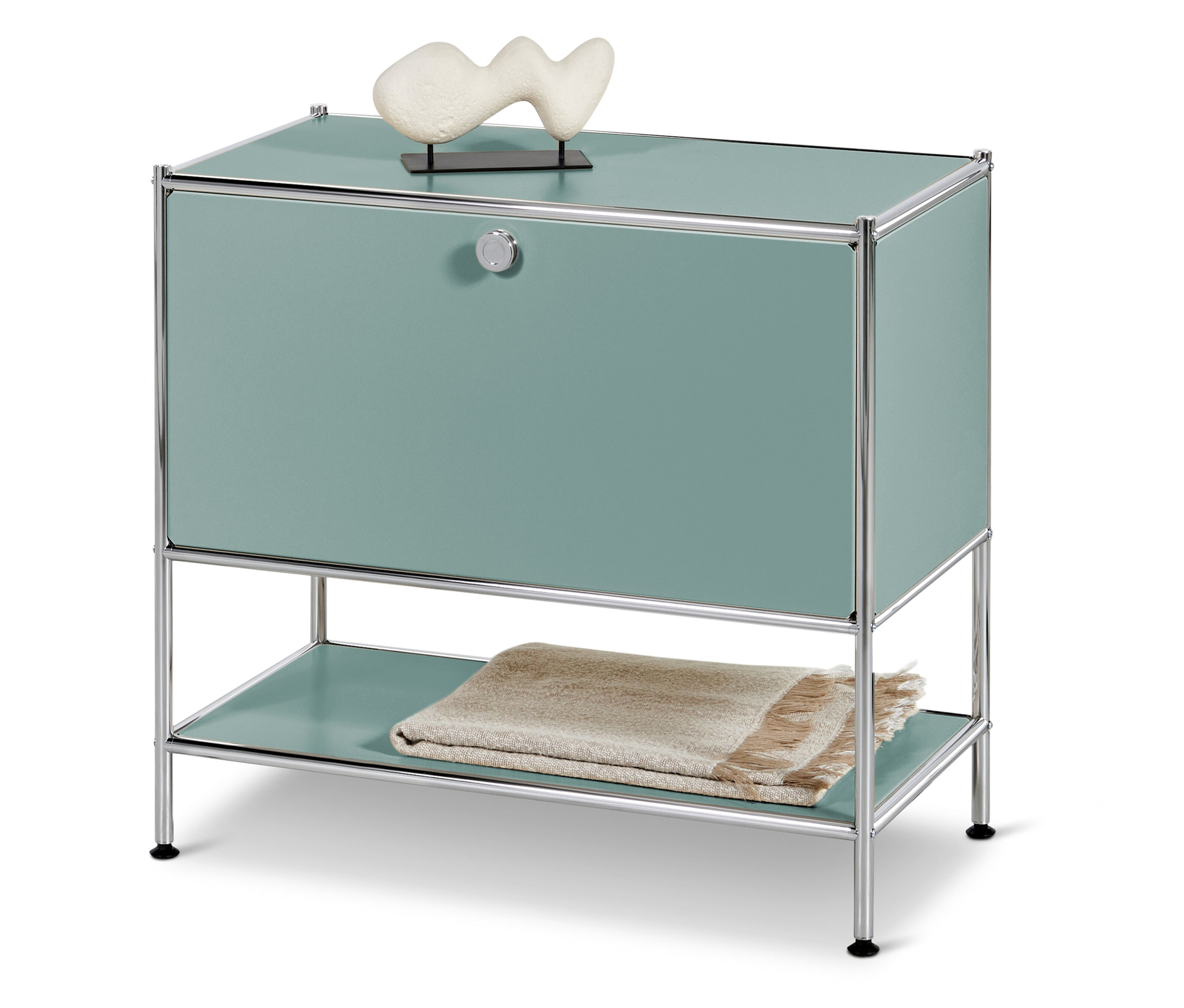 Türkiz szekrény krómvázzal, tetején fehér dísz, alatta takaró.