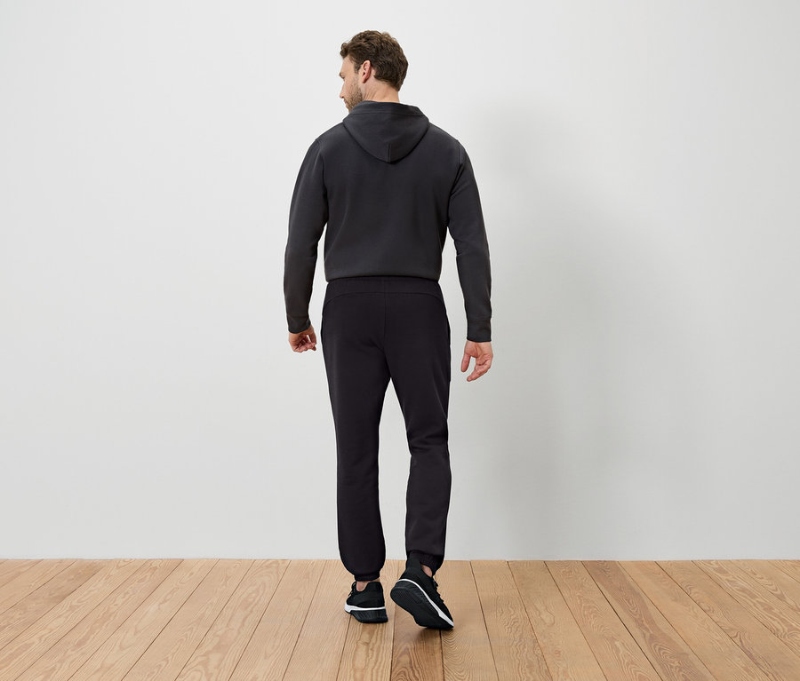 Hátulról látható férfi sötét kapucnis pulóvert és fekete melegítőnadrágot visel.