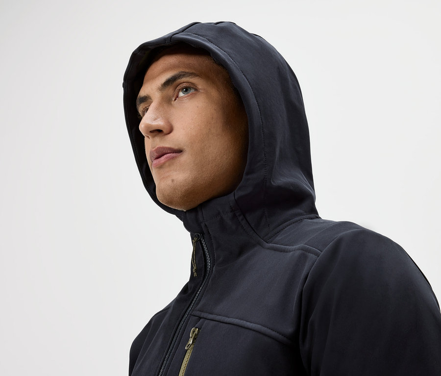 Portré egy kapucnis, cipzáras kabátot viselő férfiról, aki egy fehér háttér előtt felfelé néz.