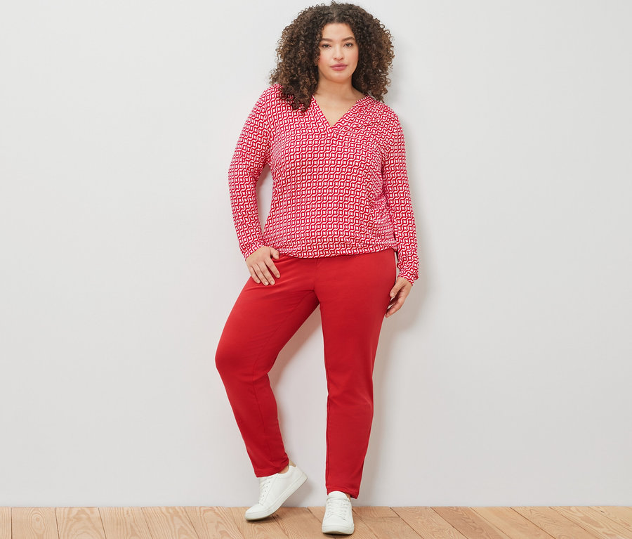 Nő pózol piros, mintás hosszú ujjú pólóblúzban és piros lezser nadrágban.