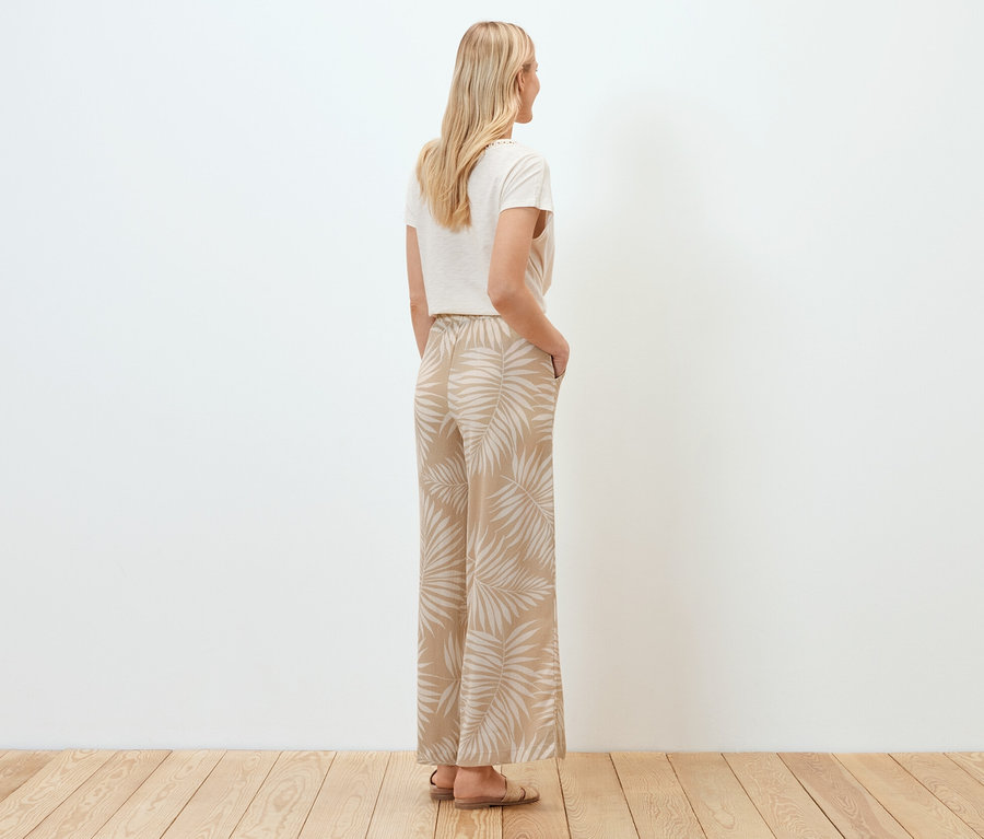 Egy nő háttal áll a kamerának, strukturált anyagú, bő szárú, nyomott mintás nadrágot visel.