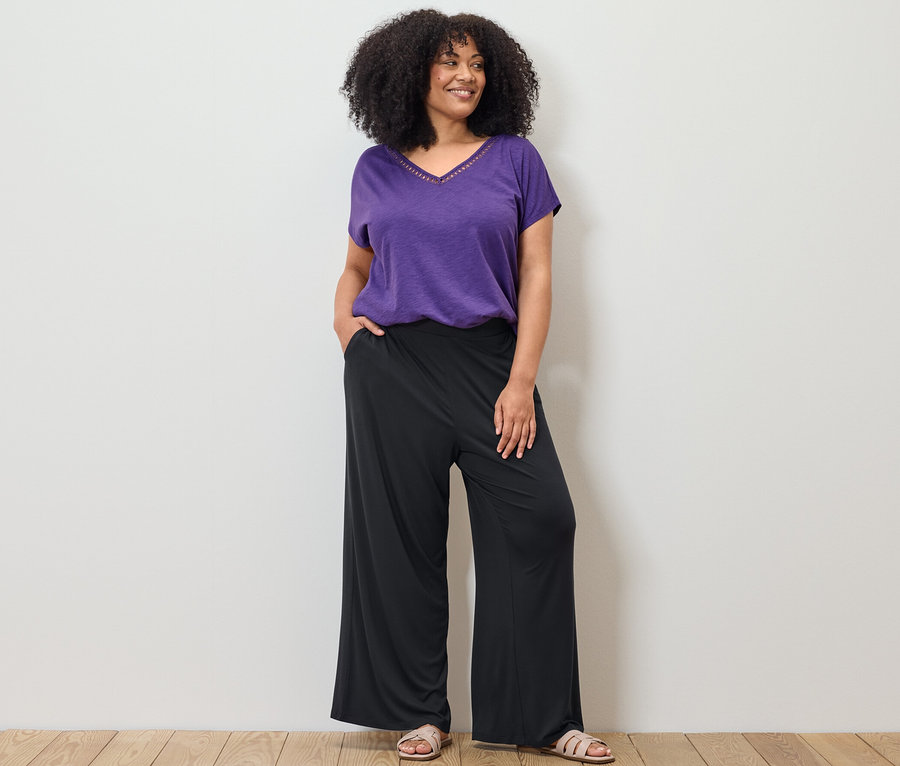 Nő pózol lila pólóban modálkeverékből és fekete palazzo nadrágban.