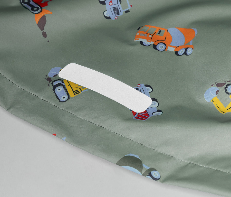 Közelkép egy olívazöld anyagról, színes építőipari járművekkel és egy fehér ragtapasszal.