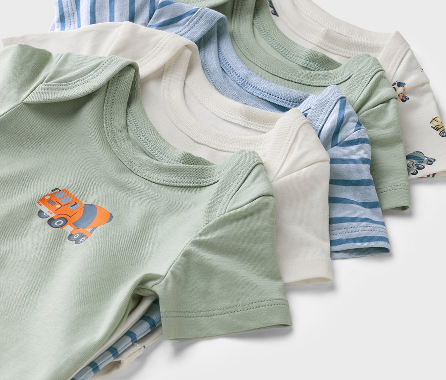 Különböző színű és mintájú rövid ujjú babaruhák közelképe, köztük egy zöld betonkeverő mintával.