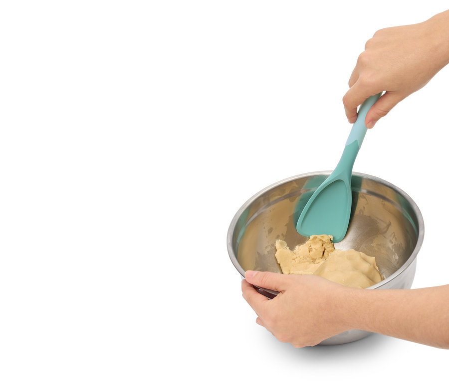 Egy személy tésztát kever egy fém tálban egy türkiz spatulával.