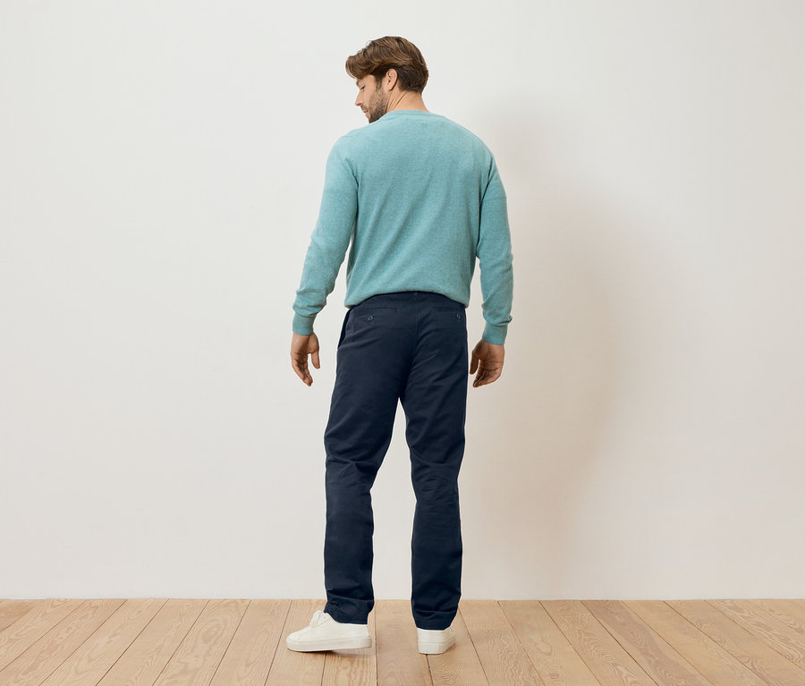 Egy férfi áll háttal a kamerának, mentaszínű pulóvert, sötétkék nadrágot és fehér tornacipőt visel.