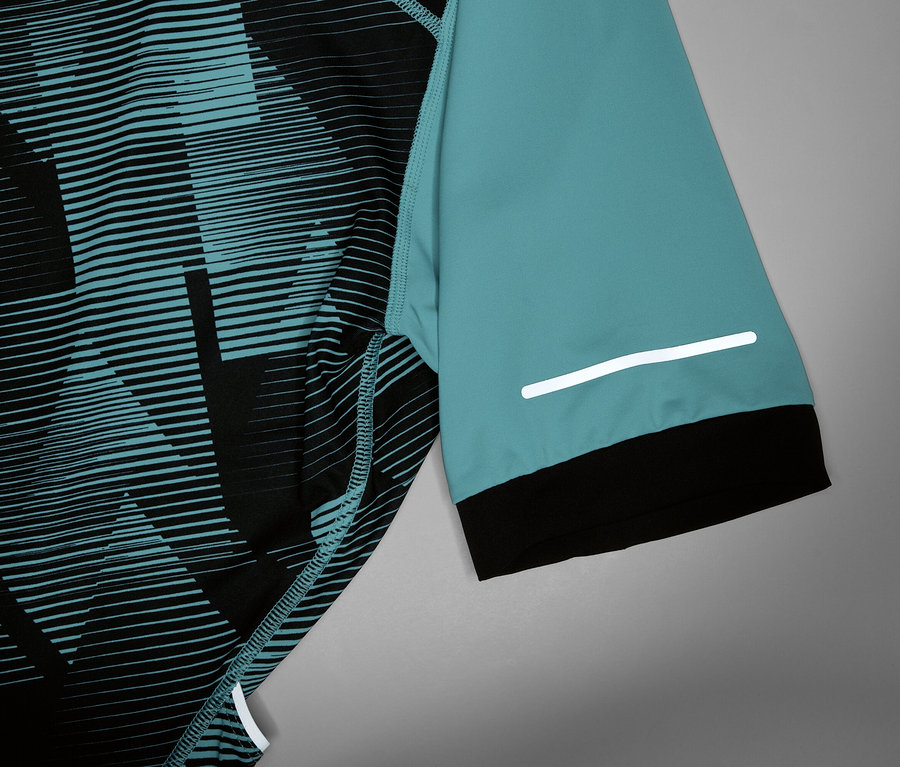 Közelkép egy türkiz ujjú, fekete mandzsettás és fényvisszaverő csíkos kerékpáros mezről.