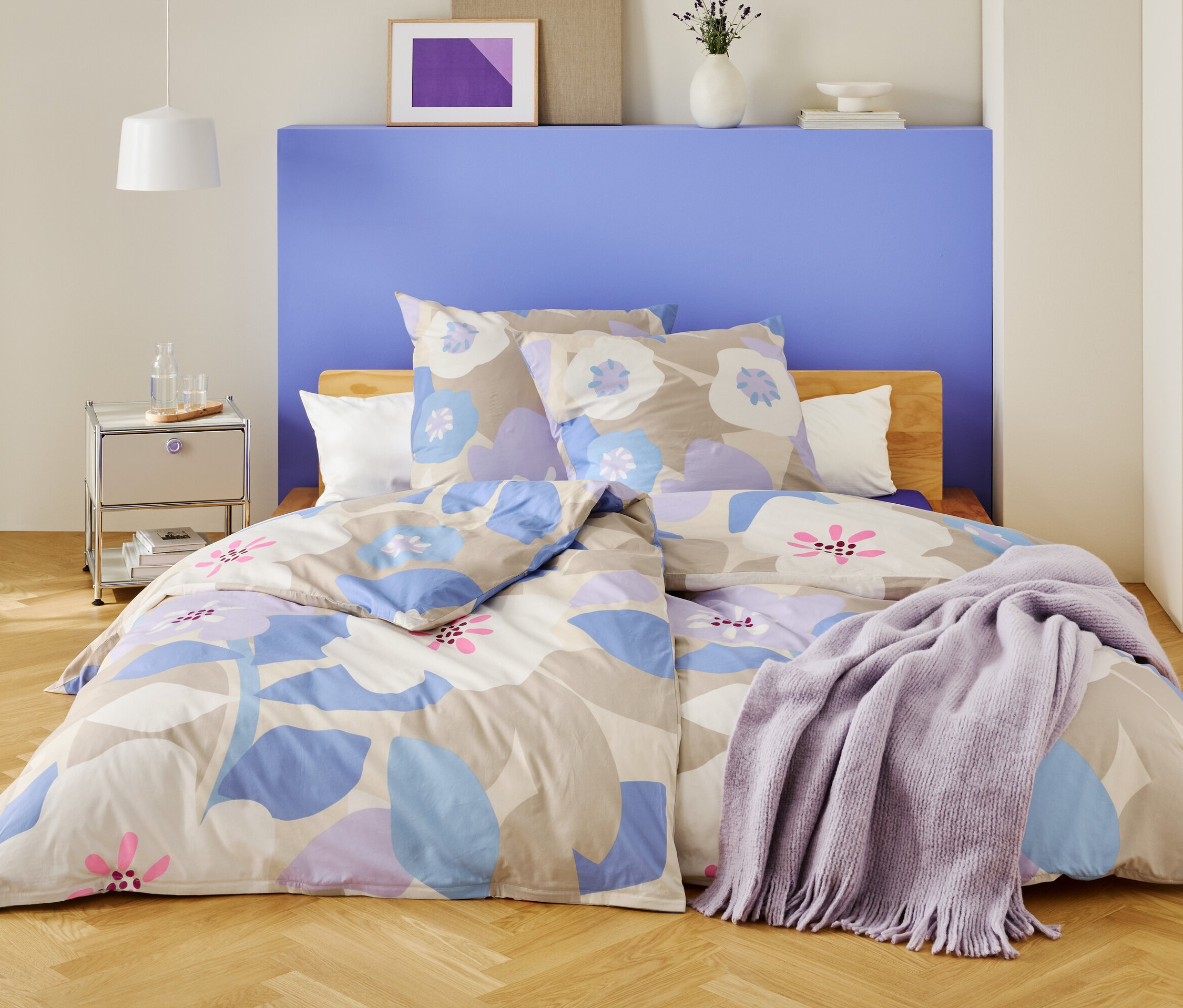 Hálószoba virágos ágyneművel és lila takaróval letakart ággyal.