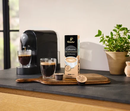 Kávéfőző kávét önt egy pohárba egy csomag Cafissimo Decaffeinato kapszula mellett.