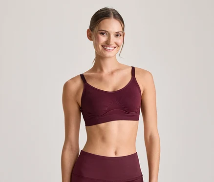 Mosolygó nő bordó sportmelltartóban és hozzá illő leggingsben, a kamerába néz.