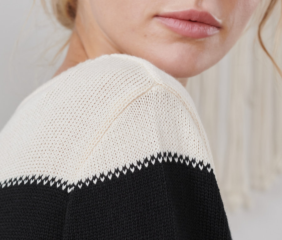 Egy fiatal nő részlete, aki egy csíkos, fekete/krém kötött pulóvert visel.