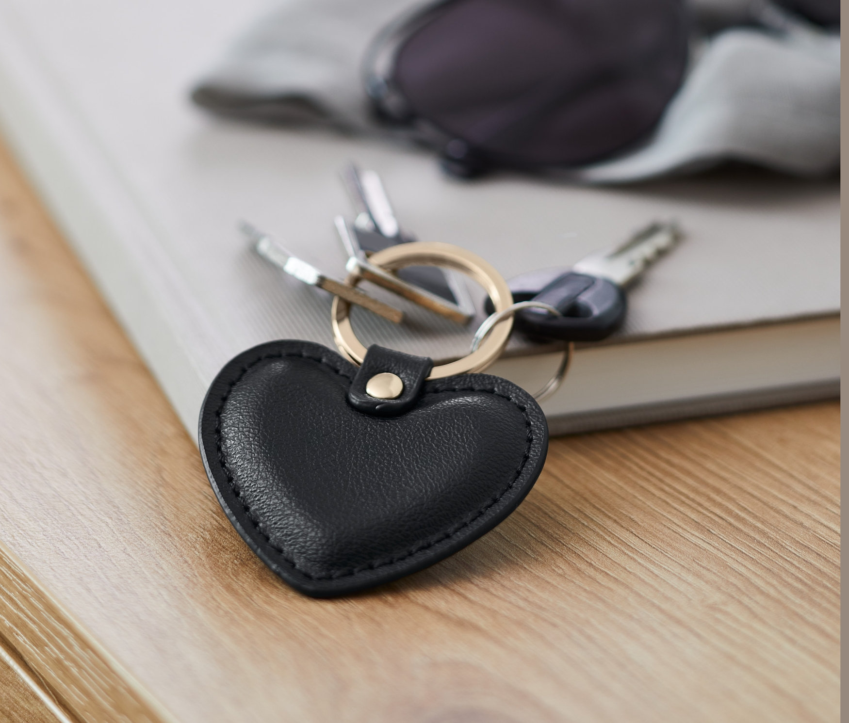 Fekete, szív alakú kulcstartó fekszik egy könyvön egy napszemüveg mellett.