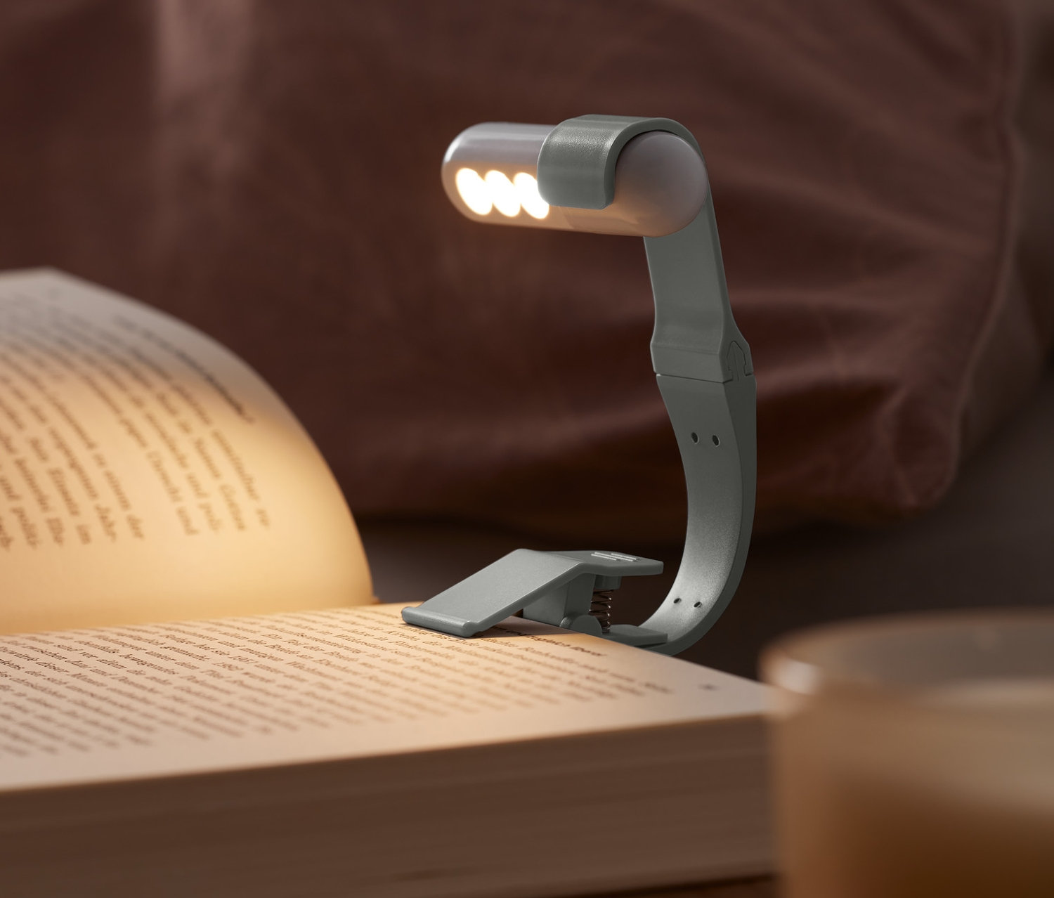 Akkumulátoros LED olvasólámpa egy könyvre van csíptetve egy éjjeliszekrényen.