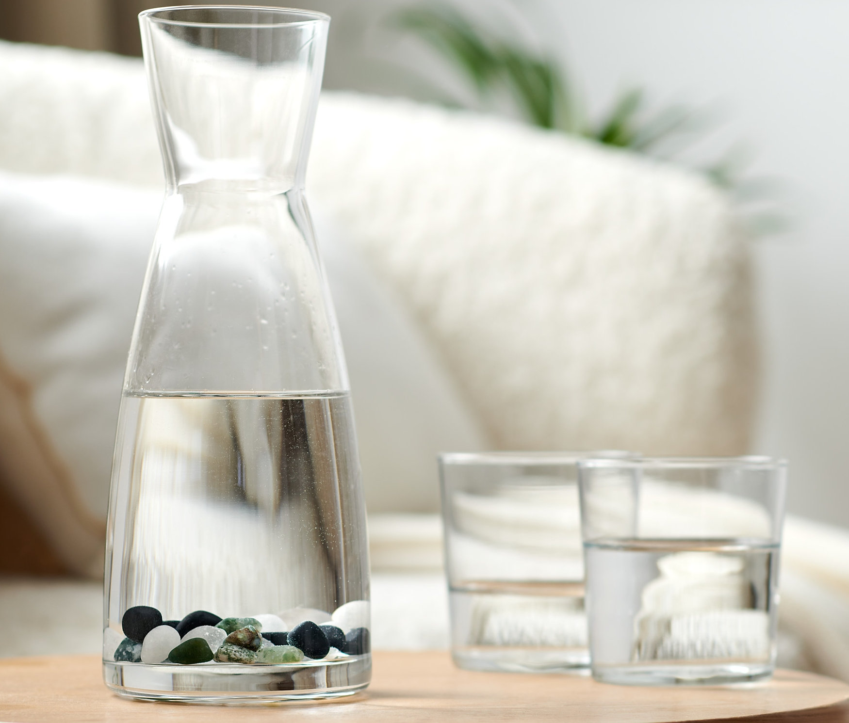 Üveg kancsó vízzel és Energetizáló kövek vízhez egy fa asztalon.