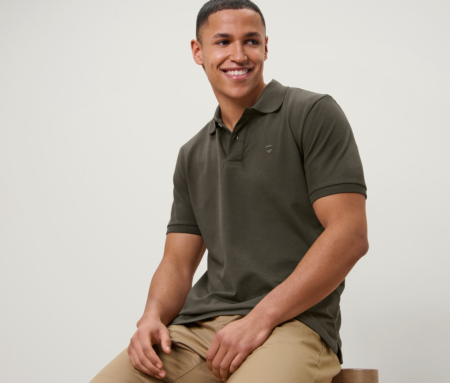 Egy férfi ül egy széken, olíva színű piké pólót és bézs rövidnadrágot visel.