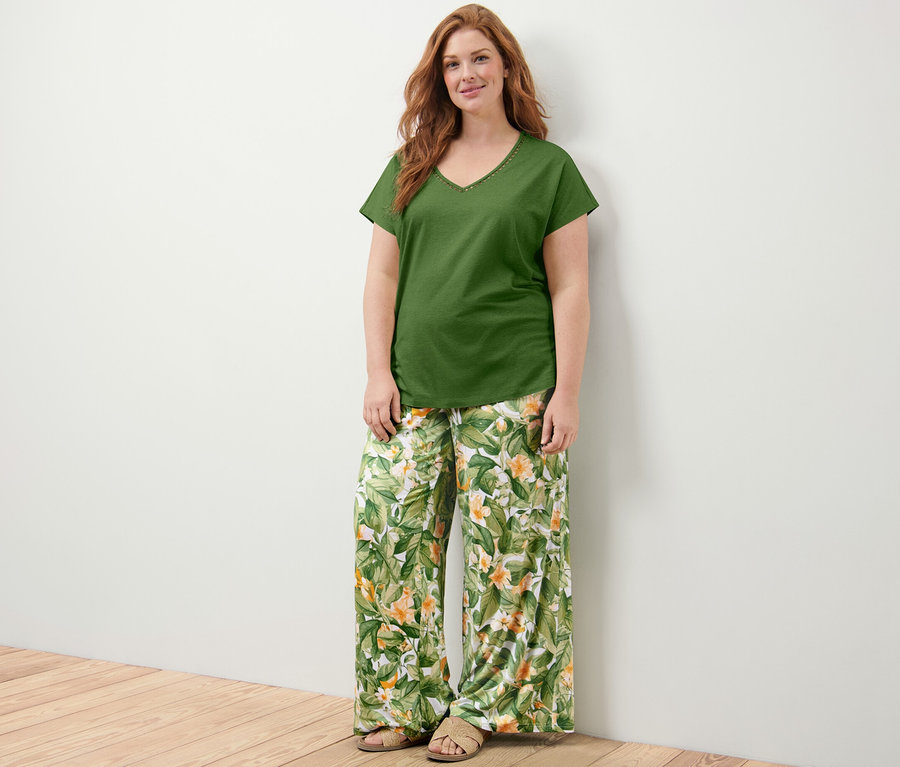 Nő áll, zöld, horgolt díszítésű pólóblúzt és nyomott mintás palazzo nadrágot visel.