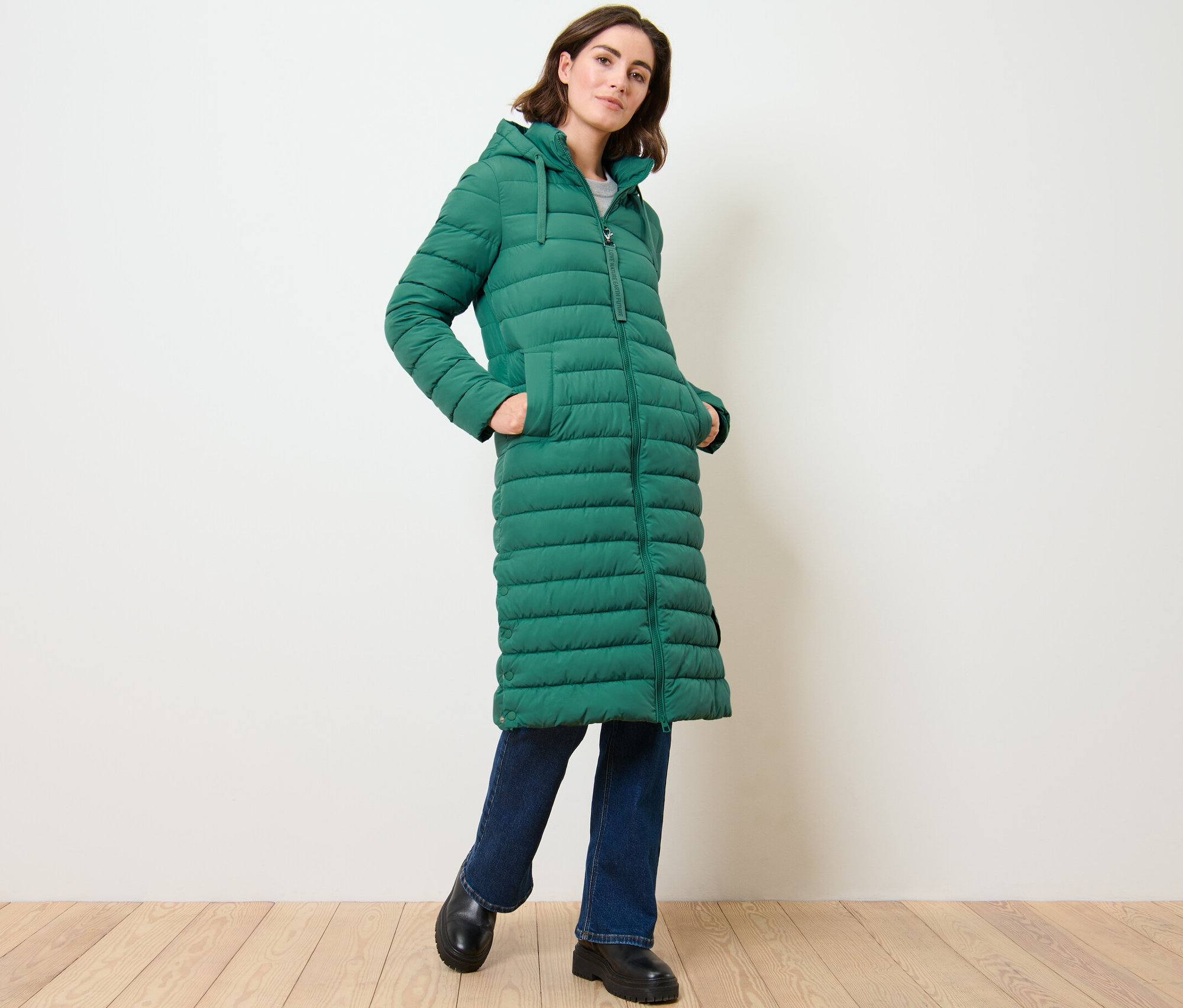 Nő pózol egy hosszú, steppelt, kapucnis kabátban.