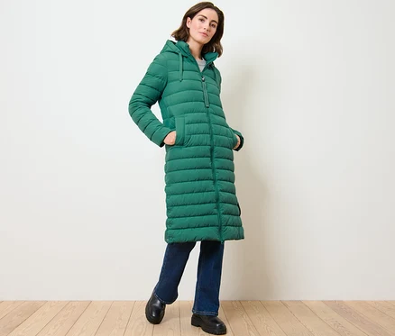 Nő pózol egy hosszú, steppelt, kapucnis kabátban.