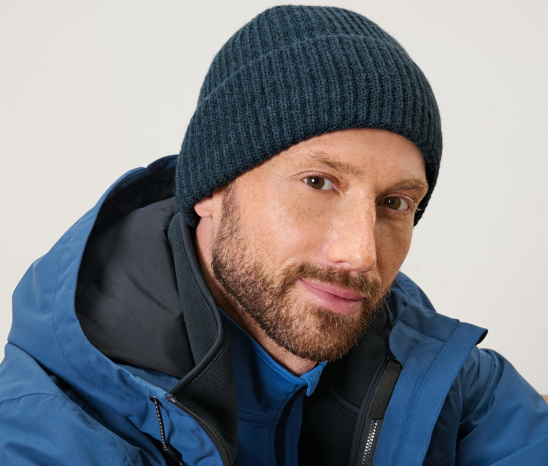 Szakállas férfi kék kötött sapkát és kék kabátot visel.