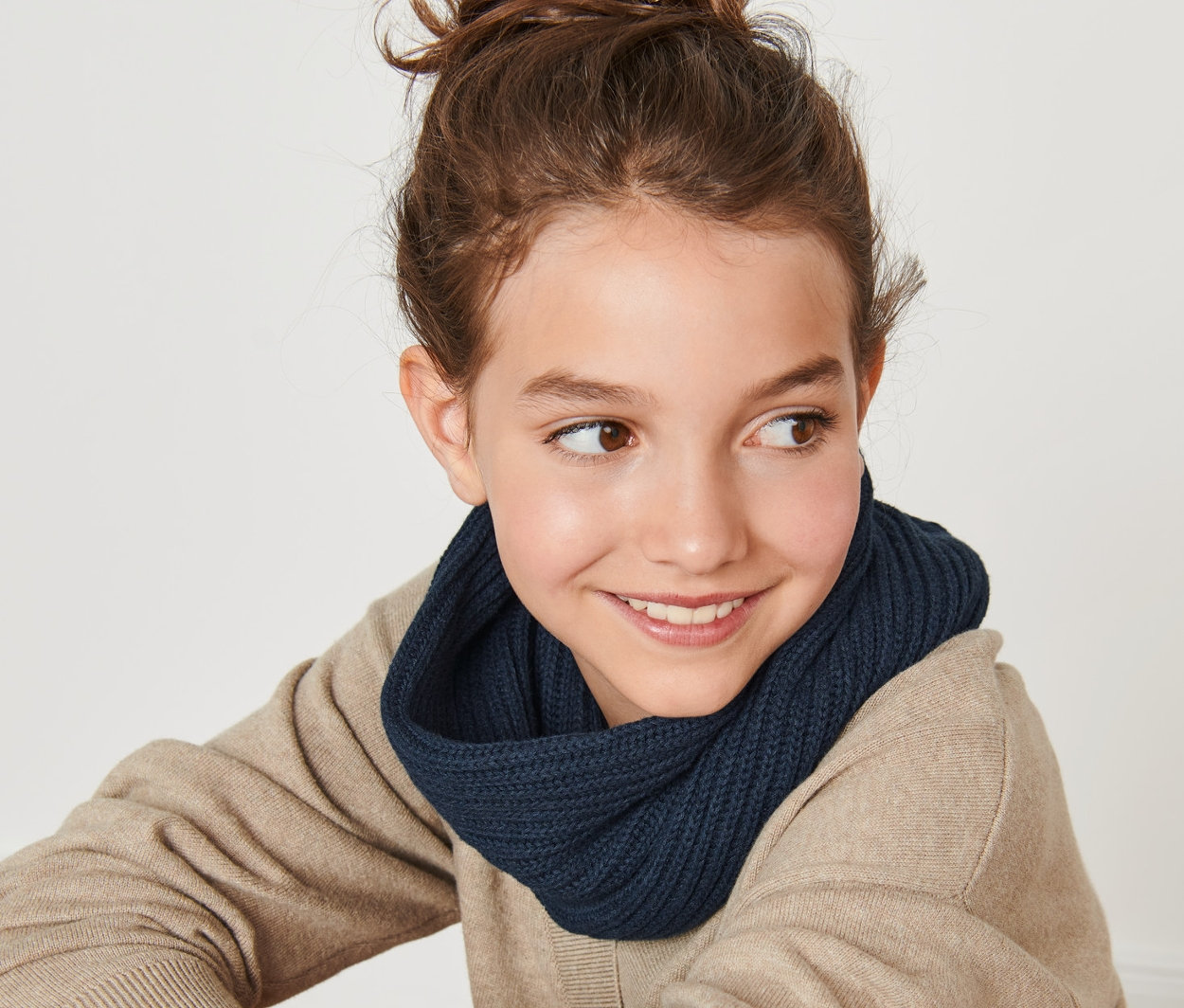 Mosolygó tinédzser lány ül háttal a kamerának, és sötétkék gyerek csősálat visel.