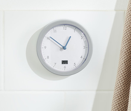 Egy fürdőszobai falióra lóg a falon egy fa létra mellett, rajta egy bézs törölközővel.