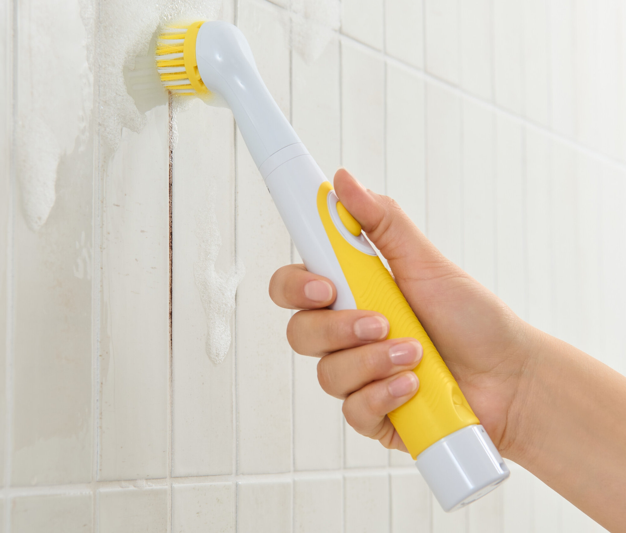 Egy kéz elektromos tisztítókefét használ a piszkos csempéken.