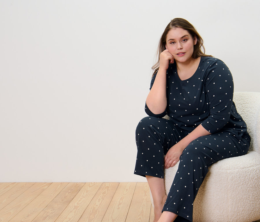 Nő ül a fotelben, sötétkék pöttyös pizsamában.
