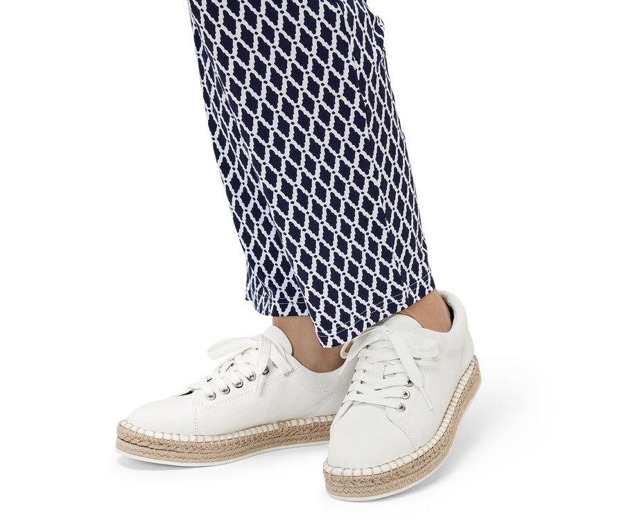 Kék-fehér mintás nadrágot és fehér női vászon sneaker cipőt viselő lábak.