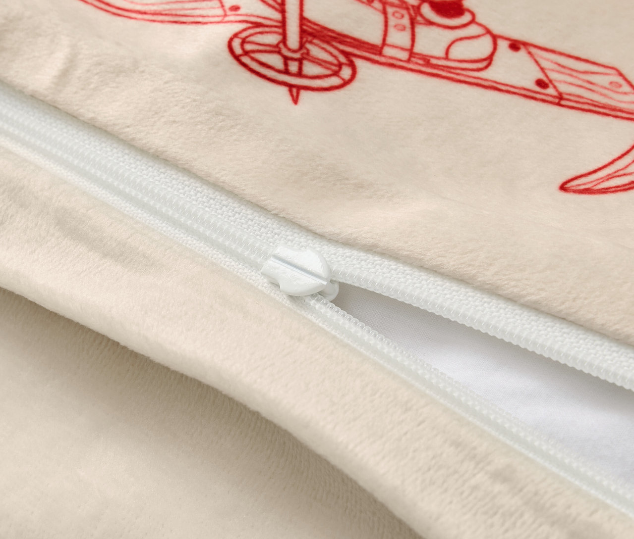 Bézs színű párnahuzat piros síelő illusztrációval és fehér cipzárral.