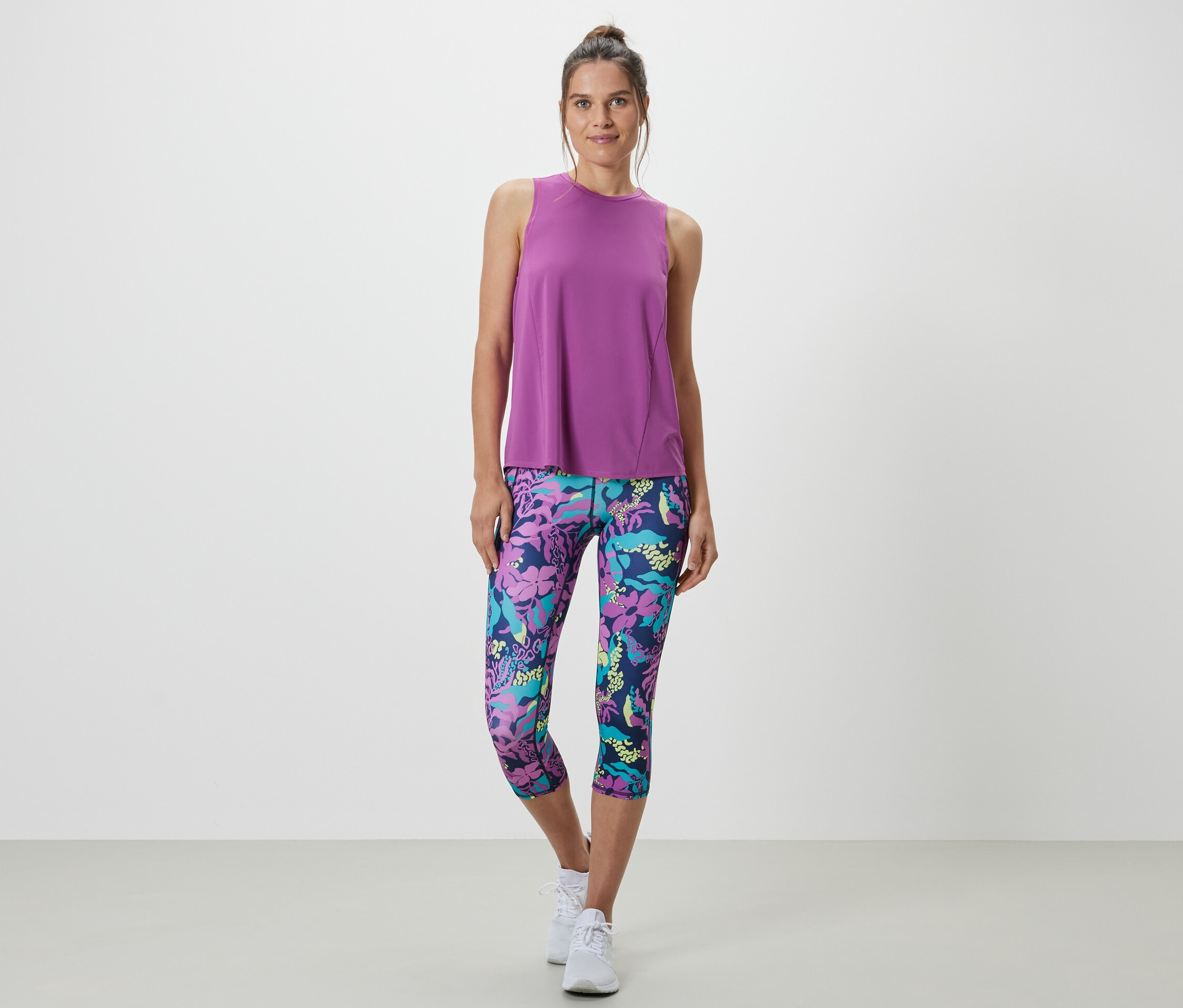 Nő visel egy türkiz sporttopot egy kétrészes szettből és egy virágmintás leggingset.