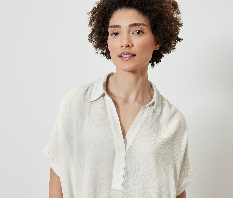 Portré egy barna, göndör hajú nőről, aki krémszínű blúzt visel.