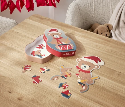 Egy Mikulás sapkás macis puzzle van szétszórva egy asztalon, mellette a doboza.