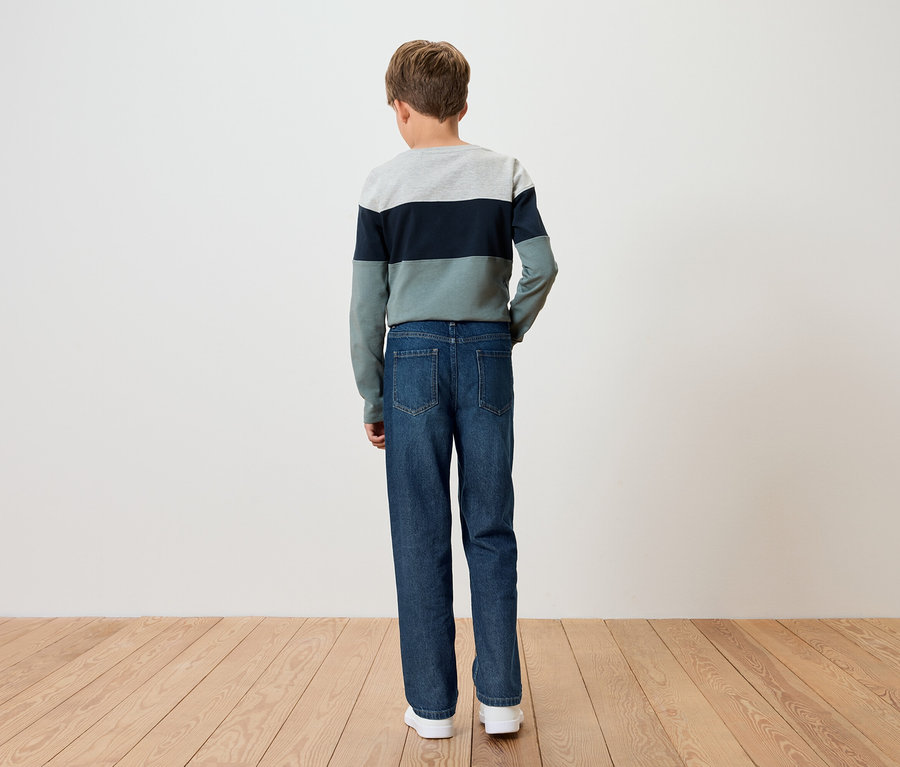 Egy fiú háttal áll a kamerának, csíkos pulóvert és kék farmert visel.
