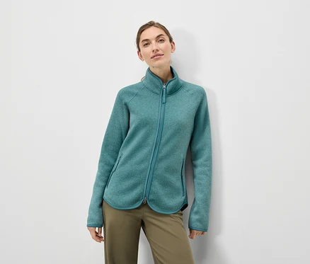 Nő visel türkiz színű fleece kabátot és olívazöld nadrágot.