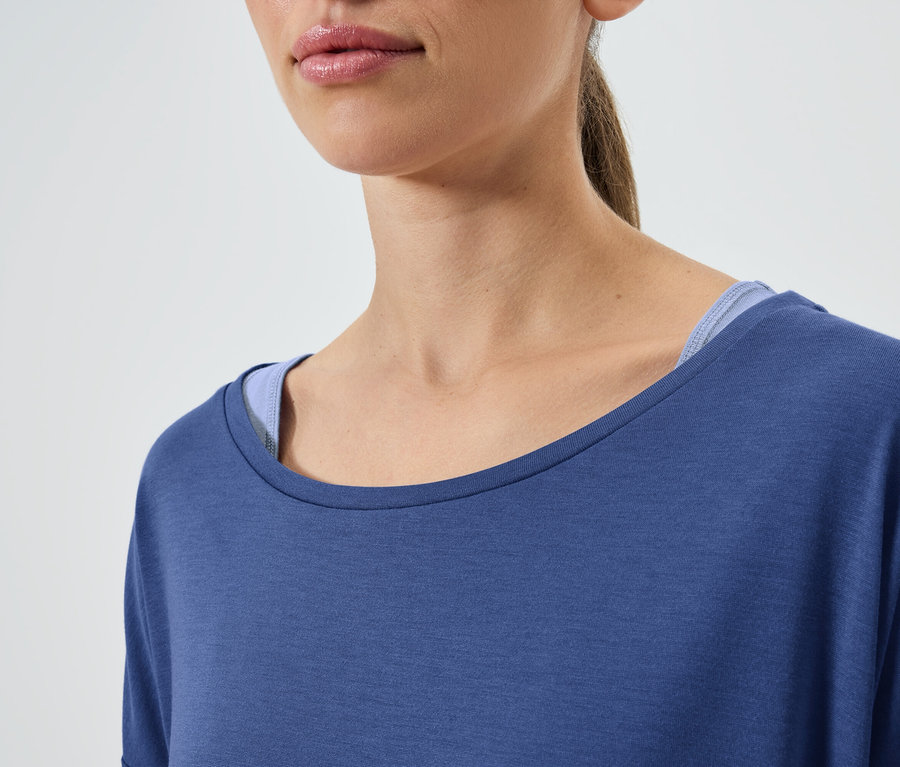 Egy barna hajú nő részlete, aki kék rövid ujjú pólót és kék trikót visel.