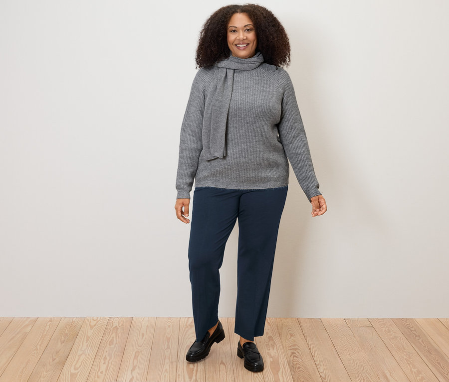 Nő szürke pulóvert és sötétkék női jersey nadrágot visel.